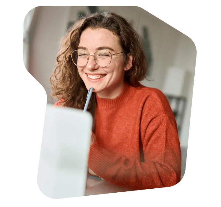 Woman Smiling and Working on a Laptop Woman in an orange sweater smiling while looking at a laptop screen.